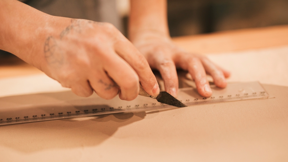 Close-up of a hand cutting clay with a tool and ruler, showing fine motor control.